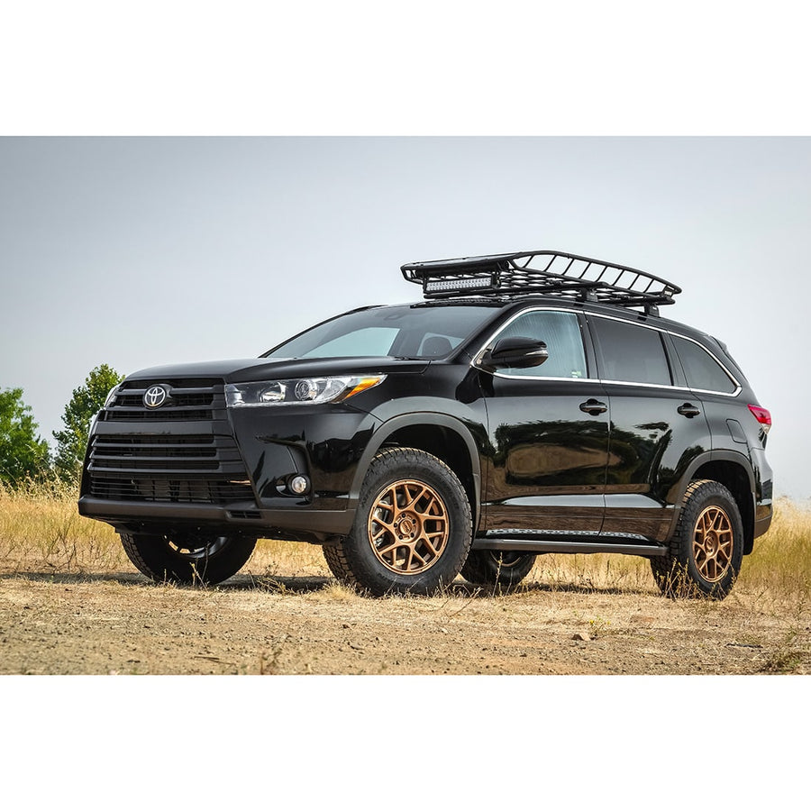 SST Lift Kits by ReadyLIFT: A black lifted Toyota Highlander with a roof basket and bronze wheels parked in a dry field.