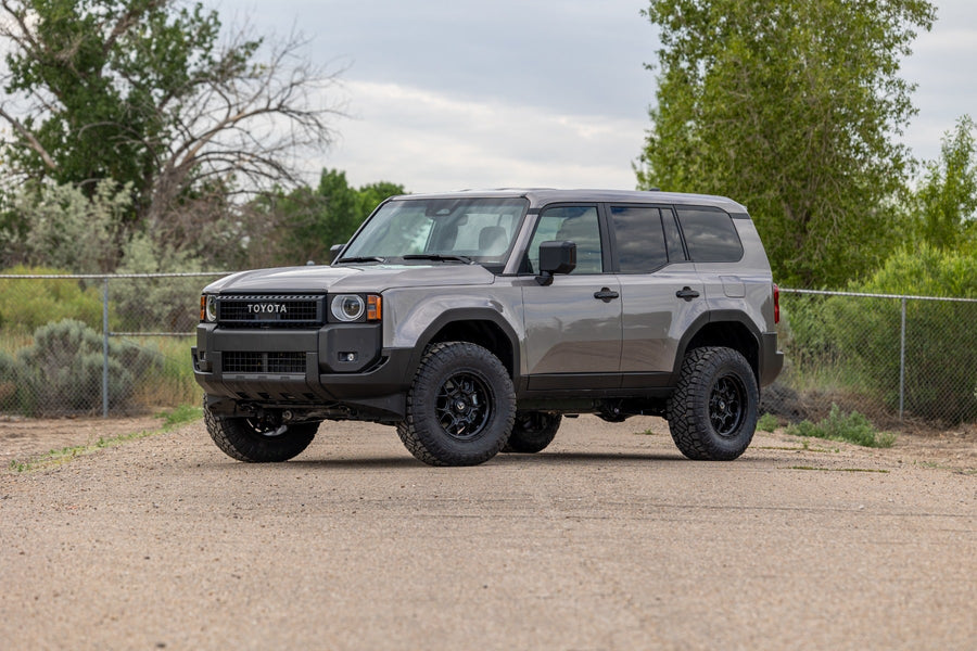 SST Lift Kits by ReadyLIFT: A gray lifted Toyota Land Cruiser parked on a gravel lot with trees behind.