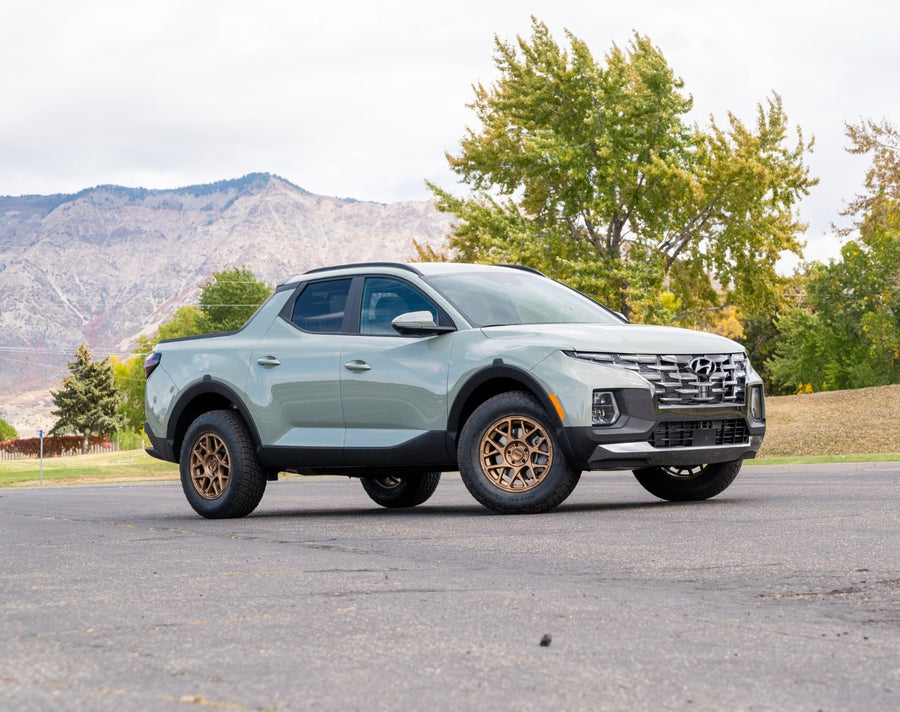 SST Lift Kits by ReadyLIFT: A sage green lifted Hyundai Santa Cruz on bronze wheels parked on pavement with trees and hills behind.