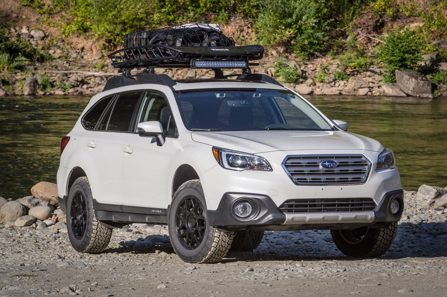 SST Lift Kits by ReadyLIFT: A white lifted Subaru Outback with a roof basket parked on a rocky riverbank.