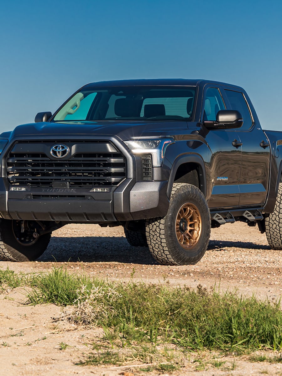 MAX Suspension Systems by ReadyLIFT: A lifted gray Toyota Tundra crew cab on bronze wheels parked in a grassy lot.