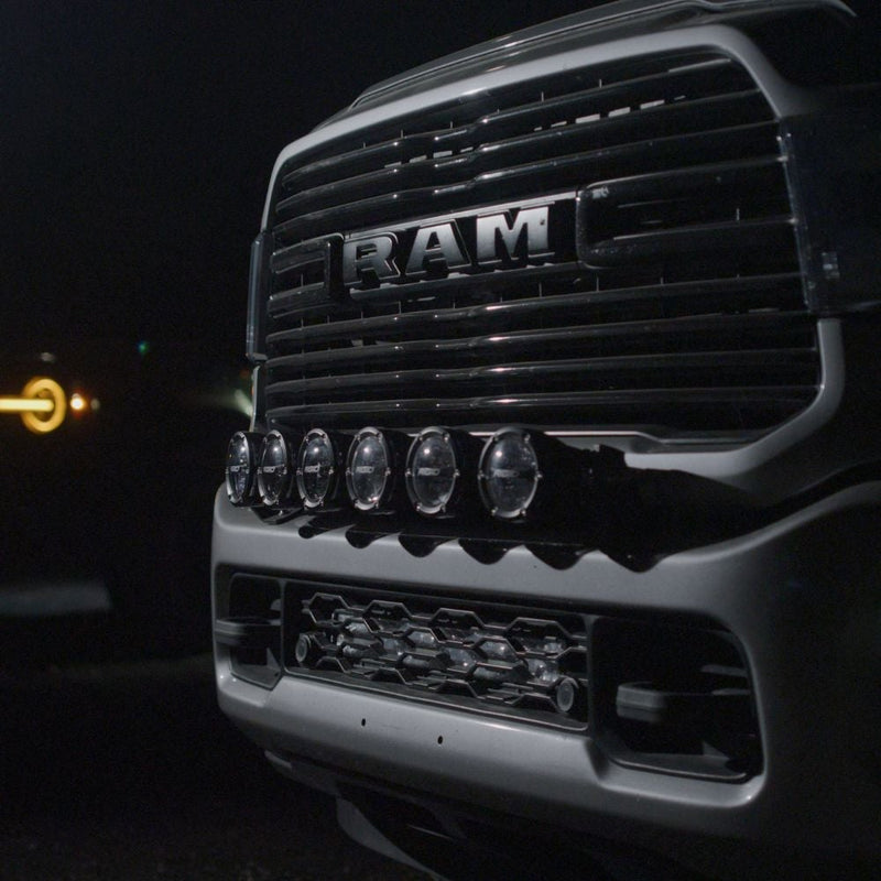 Rigid 360 Connect 30" Light Bar Assembly installed on a Ram 2500/3500 HD: night view of a Ram heavy duty pickup with RAM grille lettering and a row of round pods mounted across the front bumper
