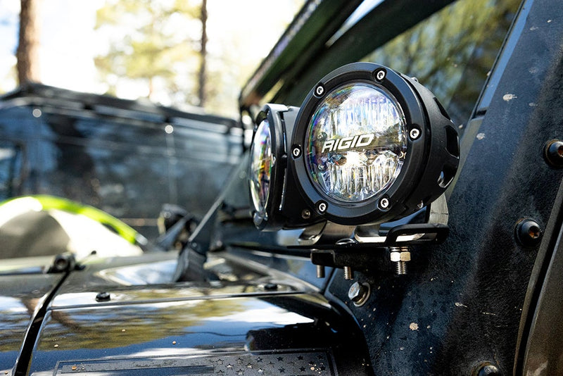 Rigid 360-Series PRO 4" Pair installed on a vehicle: two round LED lights with clear lenses sit on an A-pillar bracket of a dusty dark off-road vehicle