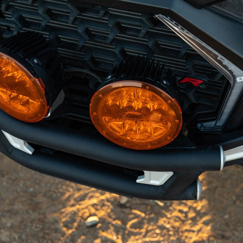 Rigid 360-Series PRO 6" Pair installed on a vehicle: two amber round LED lights mounted in a black mesh grille cast light onto the ground ahead