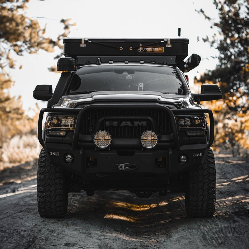 Rigid 360-Series PRO 9" installed on a Ram 2500/3500 HD: front view of a black Ram heavy duty pickup with two round LED lights mounted in its grille guard on a forest trail