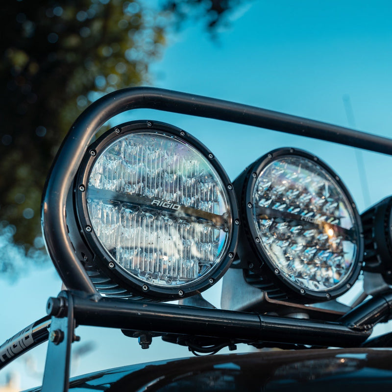 Rigid 360-Series PRO 9" installed on a vehicle: two 9" round LED lights mounted side by side on a black tubular bar above a vehicle hood against a blue sky