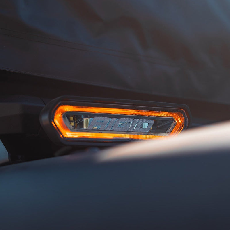 Close-up of the Rigid Chase Pod: A Chase rear light glowing amber around its halo, mounted on a dark vehicle panel at dusk