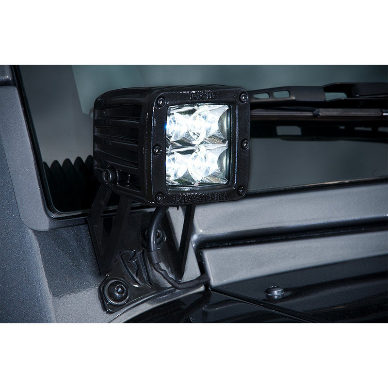 Rigid D-Series A-Pillar Mount Kit installed on a vehicle: A lit Rigid D-Series pod sits on a black bracket at the base of a windshield pillar