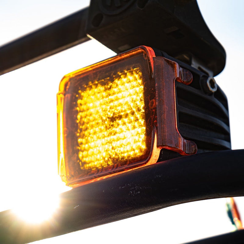 Close-up of the Rigid D-Series Cover: A D-Series pod with an amber cover glowing, mounted under a vehicle cage tube against bright sky