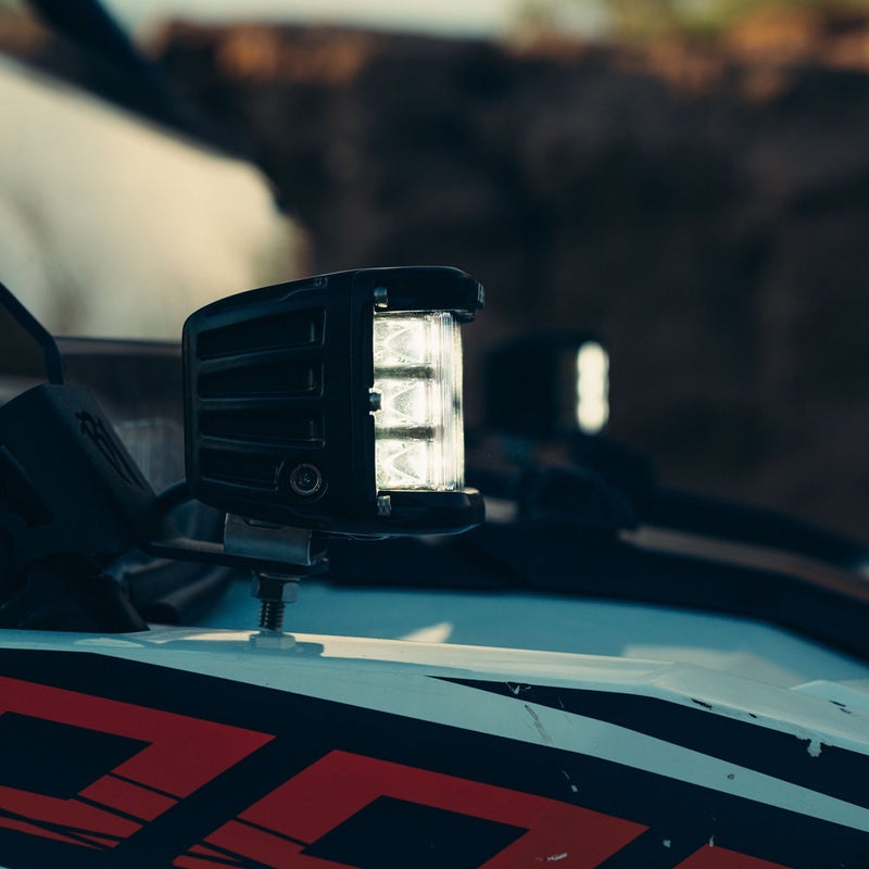 Rigid D-SS PRO Pods Pair installed on a vehicle: A D-SS side-shooter pod glows on the hood of a graphics-wrapped race truck at dusk