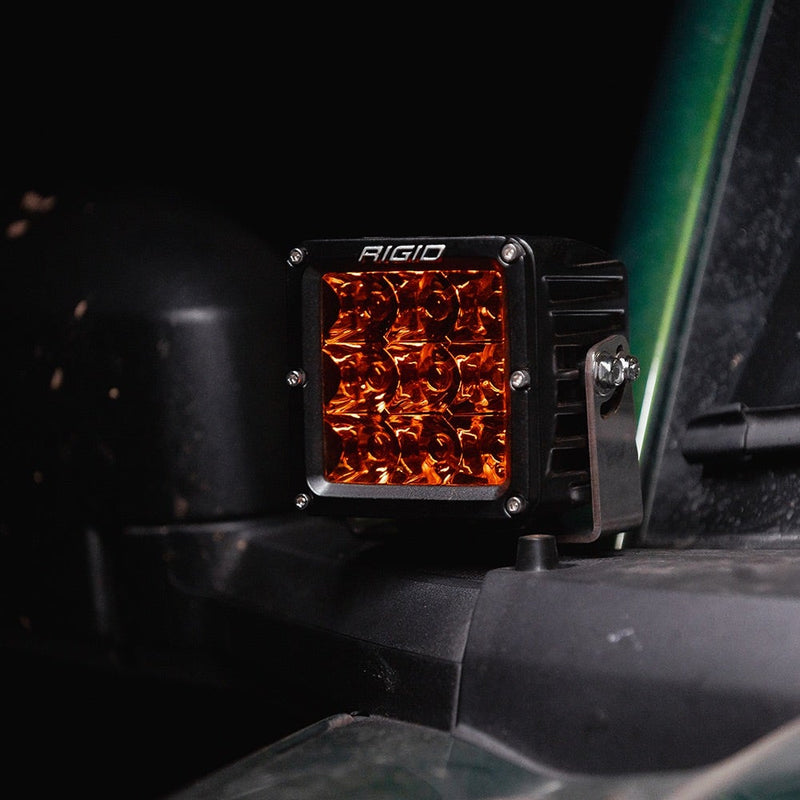Rigid D-XL PRO Pods Pair installed on a vehicle: A black D-XL PRO pod with an amber spot lens mounted on a dark vehicle's A-pillar bracket