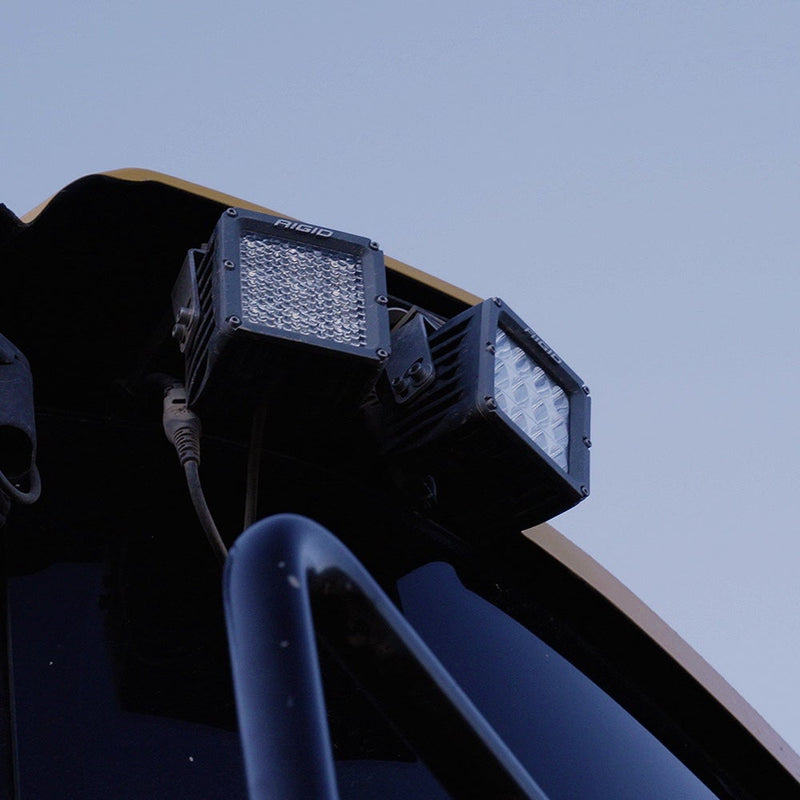 Rigid D-XL PRO Pods Pair installed on a vehicle: two black D-XL pods with diffused lenses mounted on a race vehicle roof against a blue sky