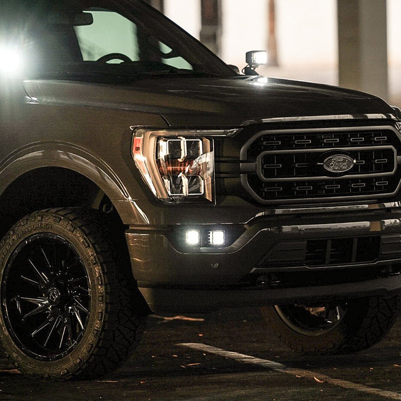 Rigid Dual Fog Light Kit installed on a Ford F-150: dark Ford F-150 at dusk with lit square pods in the fog pocket and a lit A-pillar pod