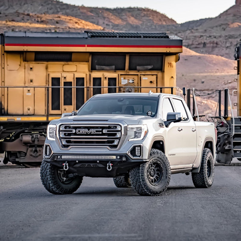 Rigid E-Series PRO 40" installed on a GMC Sierra 1500: A white GMC Sierra crew cab on black wheels with a long LED light bar in its aftermarket front bumper parked before a yellow locomotive