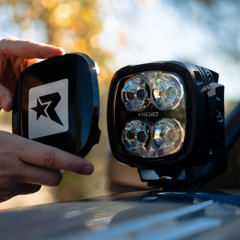 Close-up of the Rigid Phoenix Black Light Color: hands hold a black Rigid R cover beside a square quad-optic pod outdoors