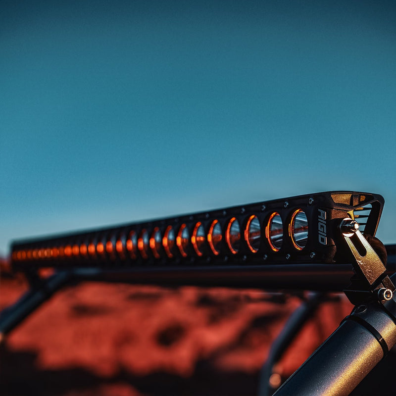 Close-up of the Rigid Revolve 50" Bar: A close-up of a Revolve light bar with amber backlighting mounted on a roll cage, red rock blurred behind