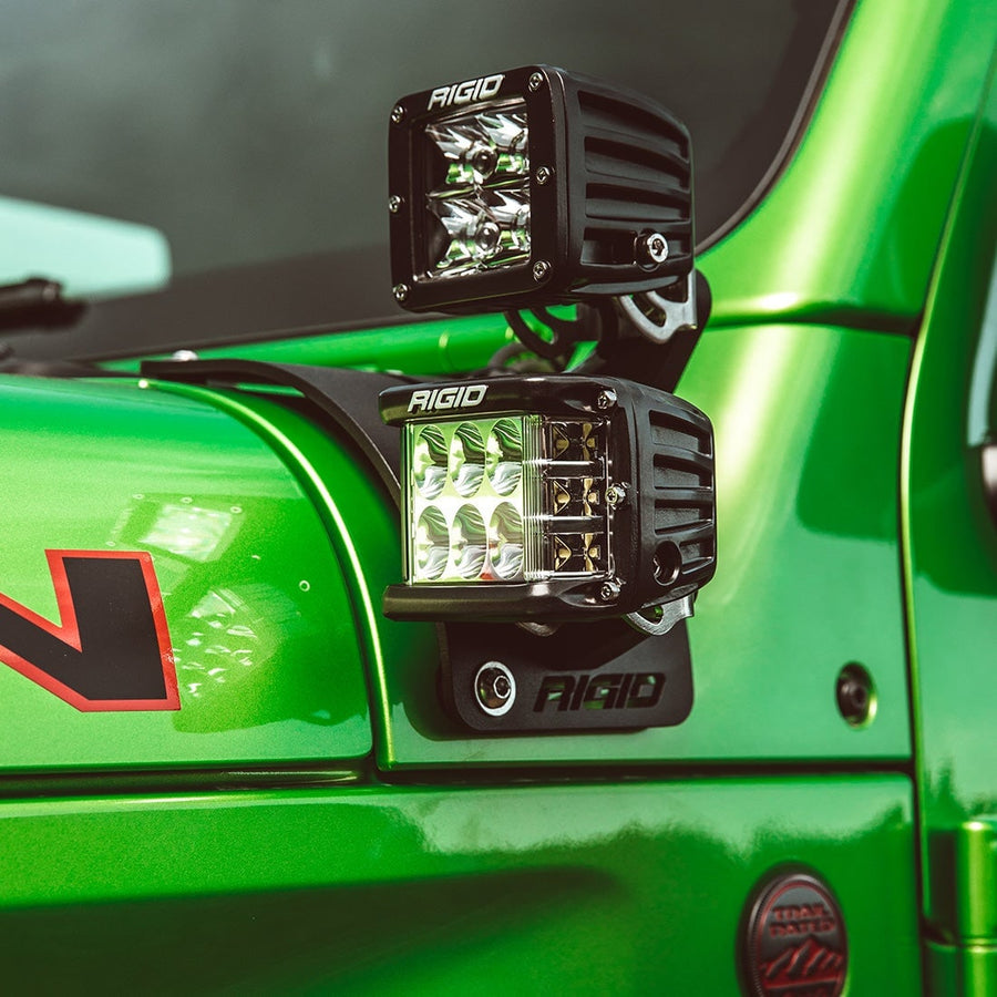Vehicle-Specific Mounts & Brackets by Rigid: Two Rigid D-Series pods sit on a cowl mount beside the windshield of a green Jeep, the lower pod lit.