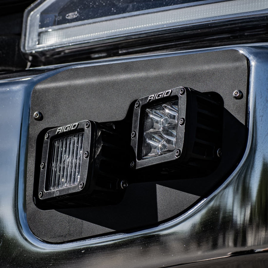 Vehicle-Specific Light Kits by Rigid: Close view of two Rigid D-Series pods set in a black fog pocket bracket on a chrome bumper.