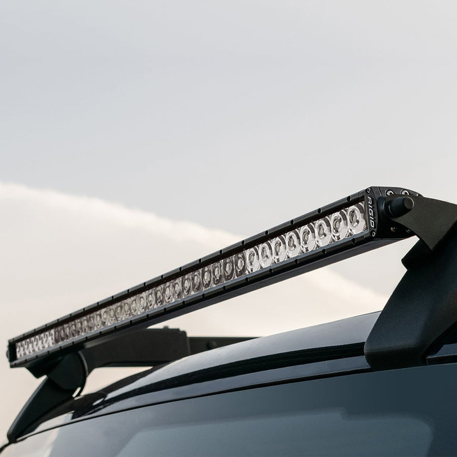 Vehicle-Specific Light Kits by Rigid: SR-Series light bar mounted on black brackets above a dark vehicle roof against an overcast sky.