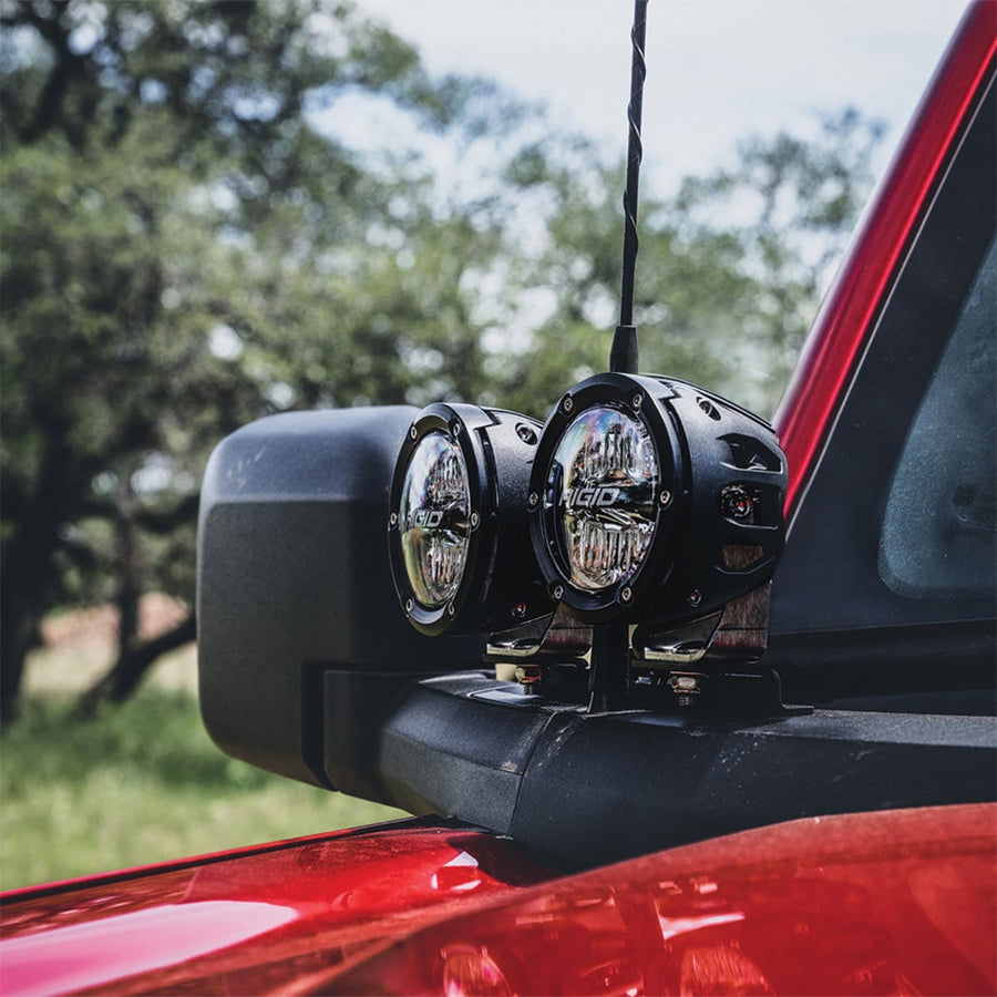 Vehicle-Specific Mounts & Brackets by Rigid: Two round black pods on an A-pillar mount next to the side mirror of a red Ford Bronco under trees.