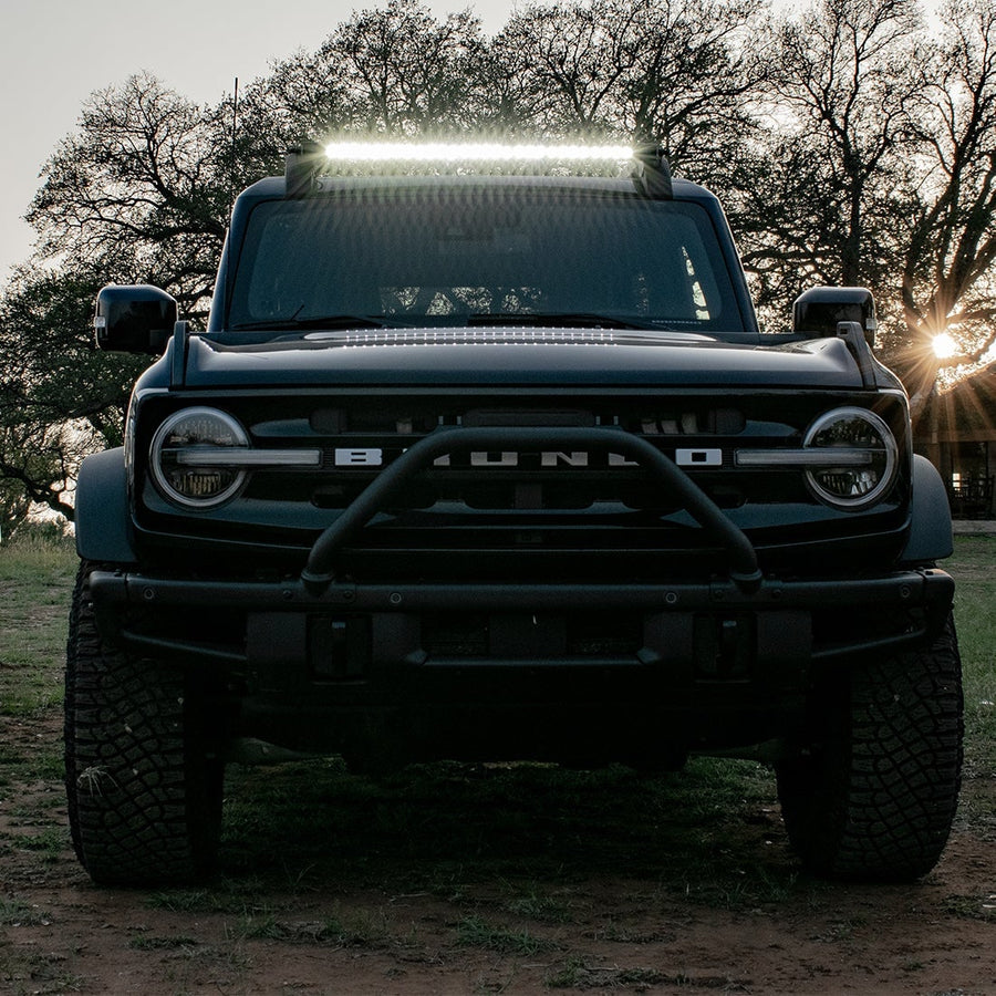 Vehicle-Specific Light Kits by Rigid: Black Ford Bronco with BRONCO grille lettering and a lit light bar across the roof at sunset.