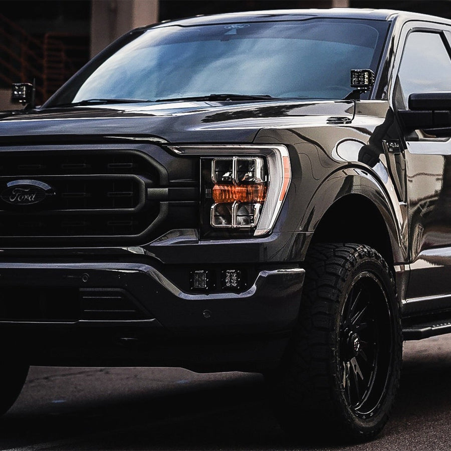 Vehicle-Specific Light Kits by Rigid: Dark gray Ford F-150 front corner with two square pods in the fog pocket and pods at the A-pillars.