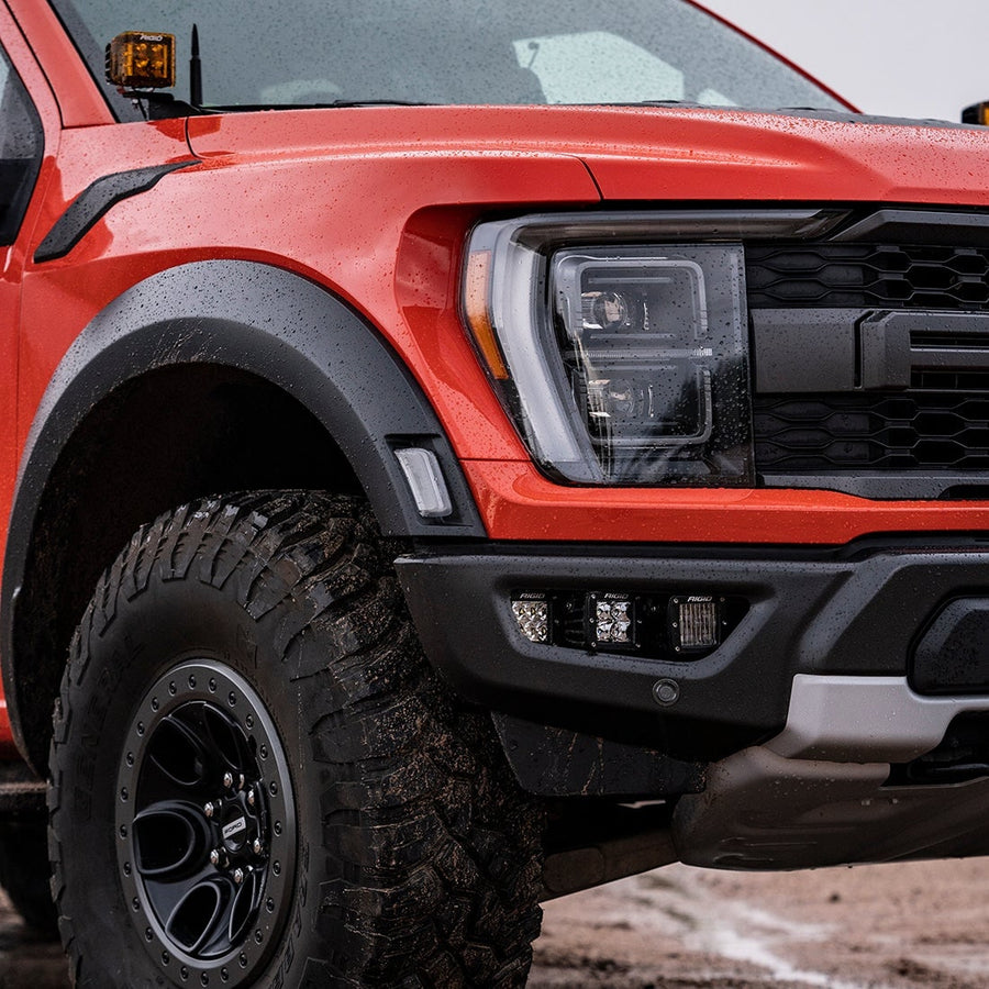 Vehicle-Specific Light Kits by Rigid: Front corner of a red Ford F-150 Raptor with square pods in the bumper opening and an amber pod at the A-pillar.