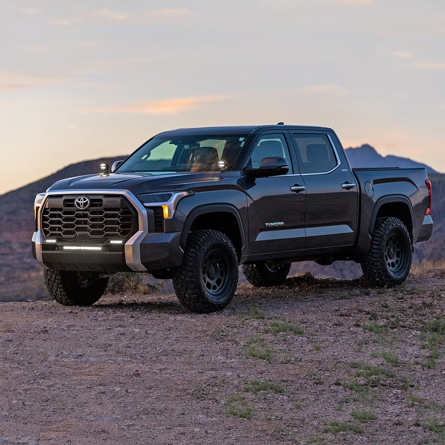 Vehicle-Specific Light Kits by Rigid: A dark gray Toyota Tundra crew cab parked on a desert hill at sunset with small round lights on both A-pillars.