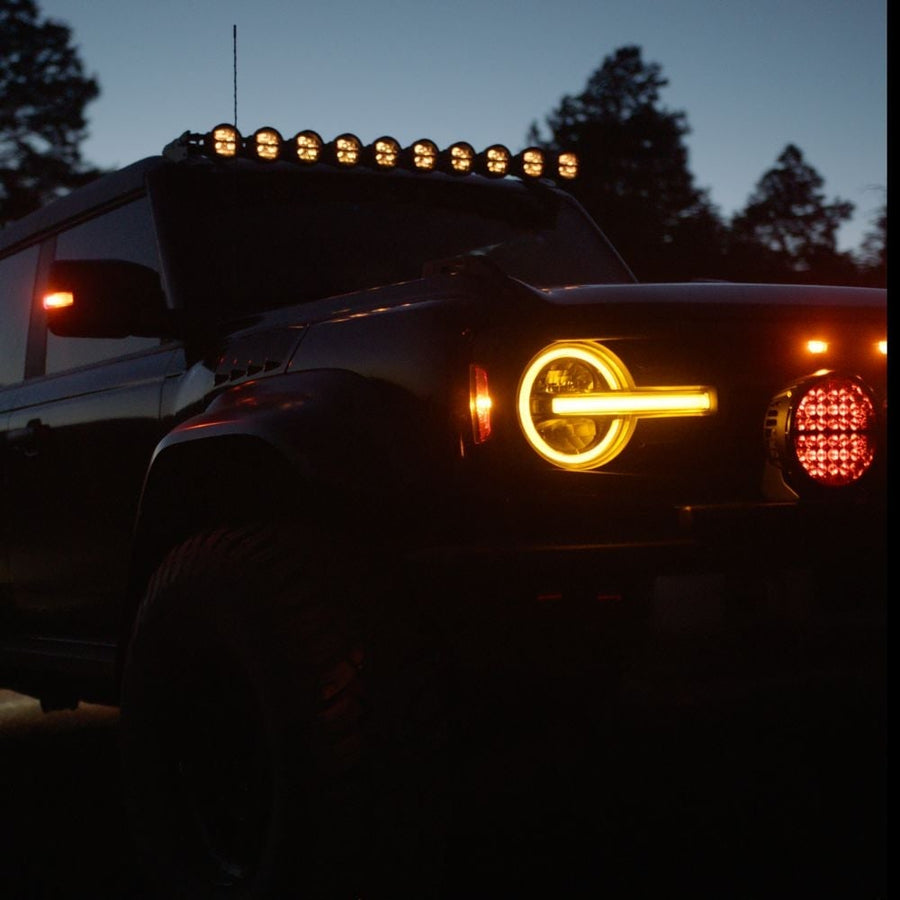 360-Series Round Lights by Rigid: A Ford Bronco at dusk with its round amber headlight signature and a lit amber ten-pod bar on the roof.