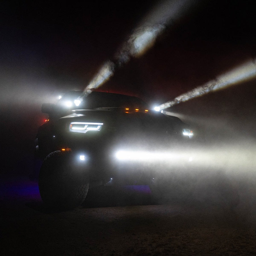 360-Series Round Lights by Rigid: A pickup at night in haze projects narrow white beams upward with a light bar glowing across its bumper.