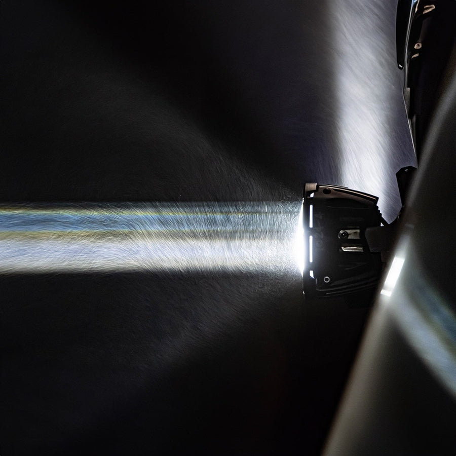 360-Series Round Lights by Rigid: A round light mounted on the side of a vehicle throws a long narrow white beam through night haze.