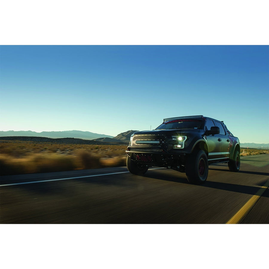 RDS SR-Series Curved Light Bars by Rigid: A dark Ford F-150 pickup with a curved roof light bar and grille light bars drives down a desert highway at dusk; the roof bar housing looks black.
