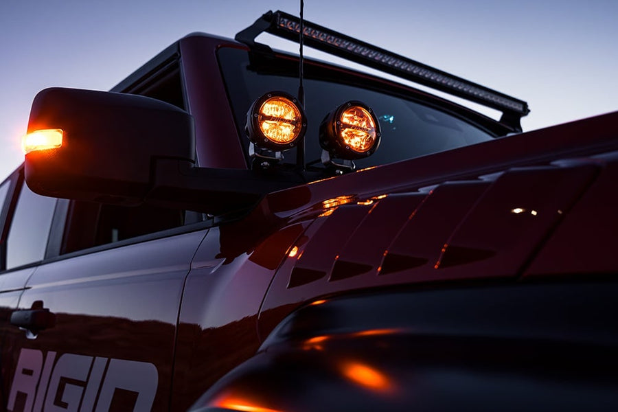 360-Series Round Lights by Rigid: Two round LED pods glow amber at the A-pillar of a dark red truck under a roof light bar at dusk.