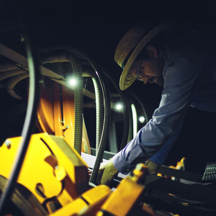 A-Series Rock & Utility Lights by Rigid: A man in a straw hat works on yellow machinery lit by small white lights in a dark compartment.