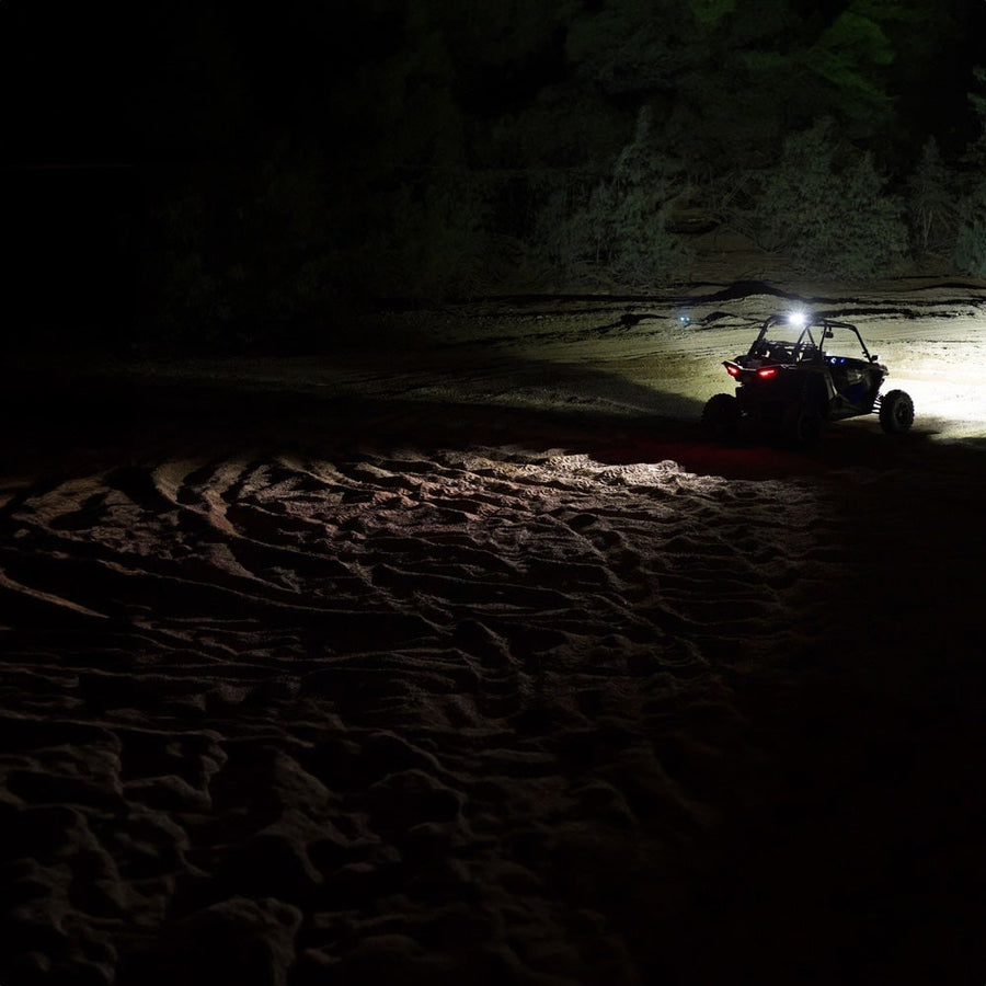 Chase Rear Lights by Rigid: A side-by-side UTV far off in dark sand dunes at night with its lights on.