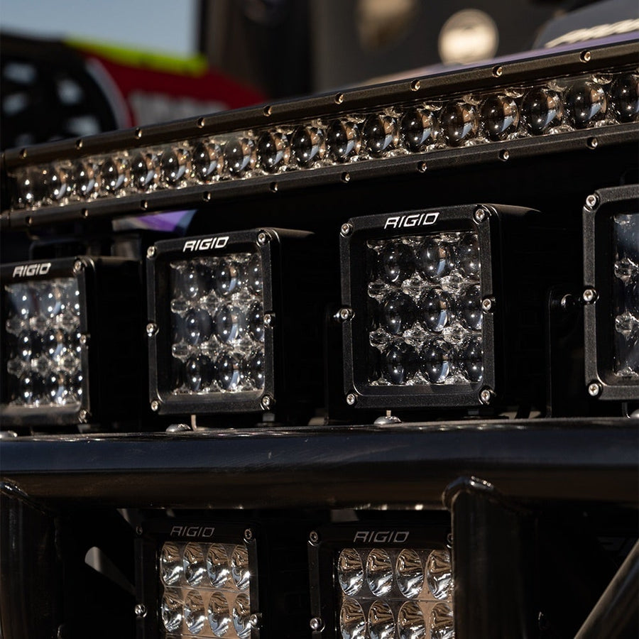 D-Series Pods by Rigid: Several black D-XL PRO pods mounted in a row on an off-road race vehicle beneath a glowing LED light bar.