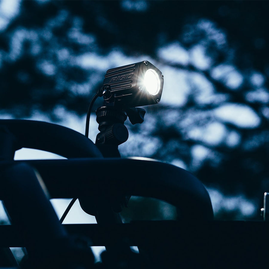 Ignite Lights by Rigid: A small black pod light glows on a rail mount at night against dark trees.