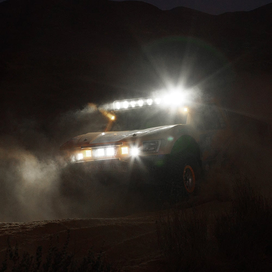 Q-Series Lights by Rigid: An off-road race truck kicks up dust at night with its roof bar and bumper lights blazing.