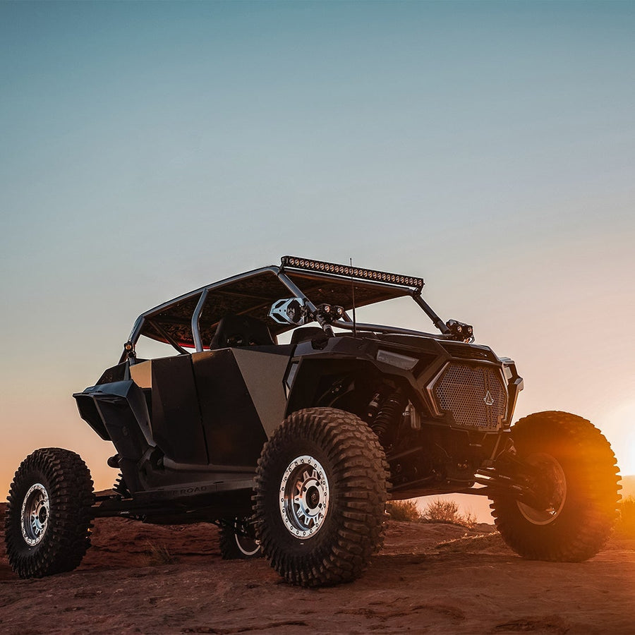 Revolve Lights by Rigid: A black Polaris RZR four-seat side-by-side with a roof light bar, backlit by the setting sun on red dirt.