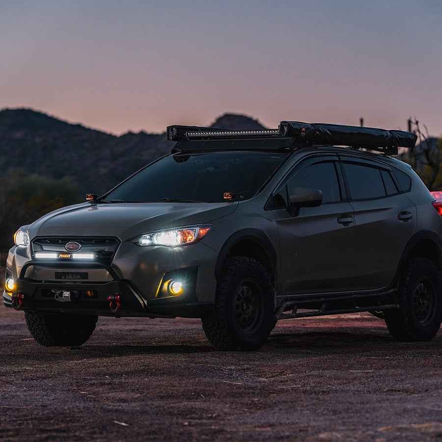 SR-Series Light Bars by Rigid: A green Subaru Crosstrek with a roof rack light bar and bumper light stands on a desert lot at dusk.