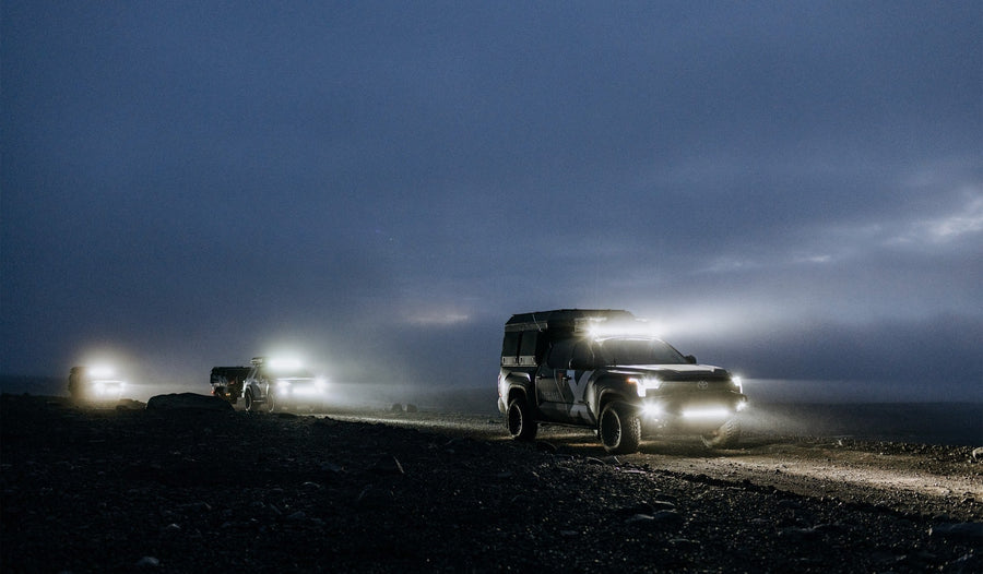 SR-Series Light Bars by Rigid: A Toyota Tundra with a camper shell leads a convoy at dusk, its bumper bar, roof bar and fog lights all lit.