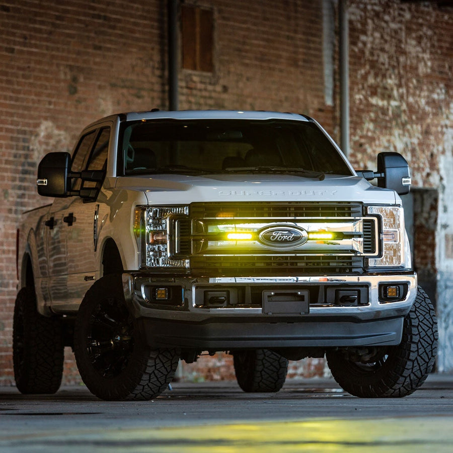 SR-Series Light Bars by Rigid: White Ford Super Duty with SUPER DUTY hood lettering parked in a brick warehouse, two selective yellow 6 inch lights glowing in the grille