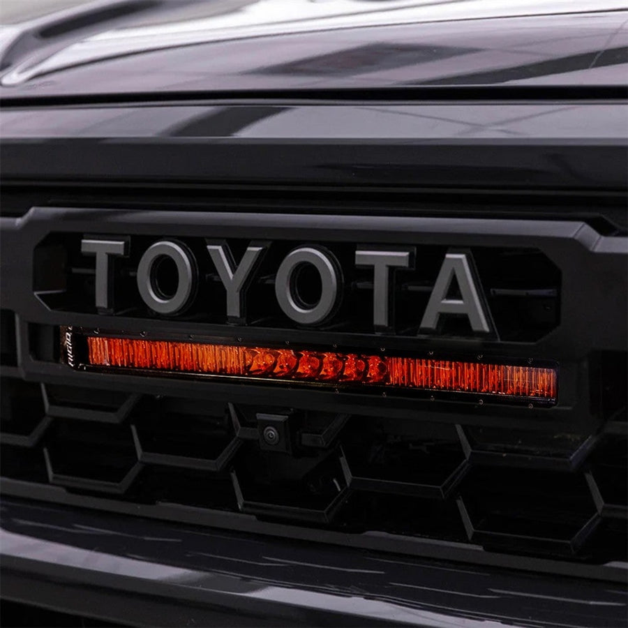 Vehicle-Specific Light Kits by Rigid: Close-up of a 20 inch amber SR-Series light bar installed under the TOYOTA lettering in a black Tacoma grille