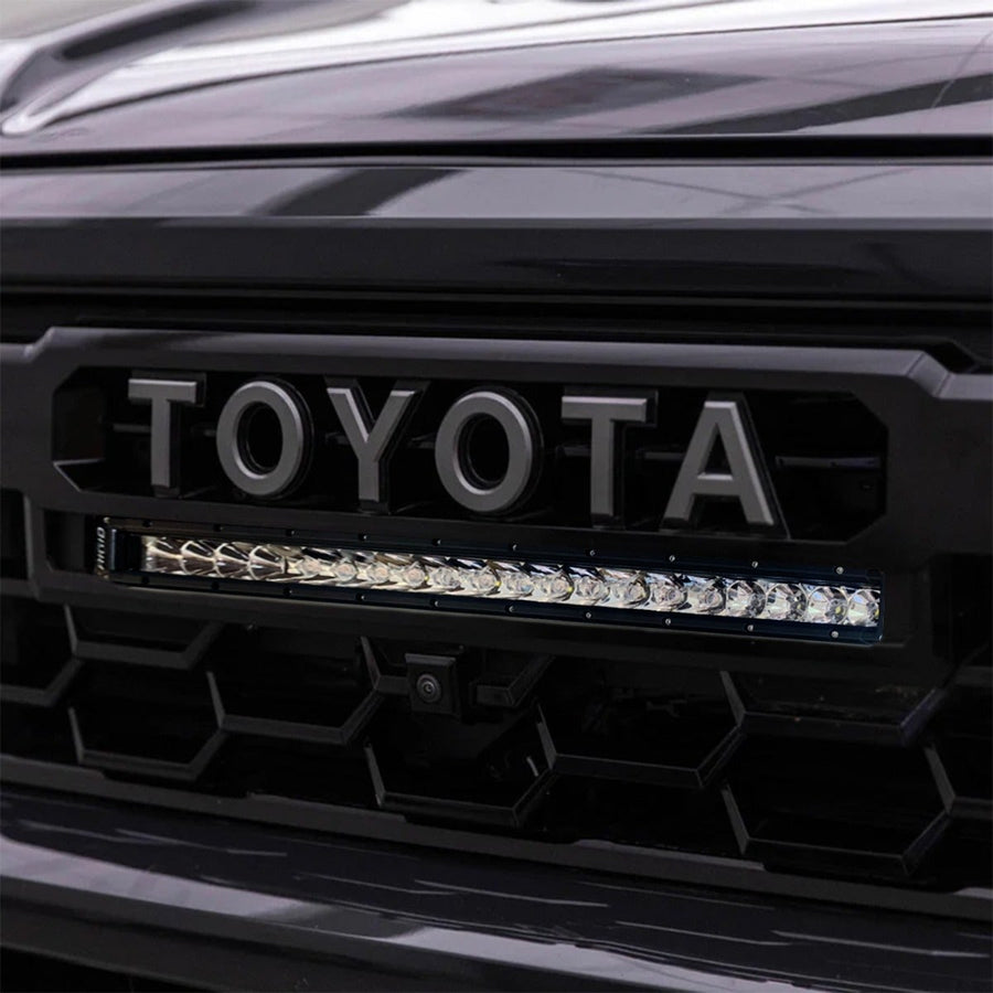 Vehicle-Specific Light Kits by Rigid: Close-up of a 20 inch SR-Series spot and flood light bar installed under the TOYOTA lettering in a black Tacoma grille