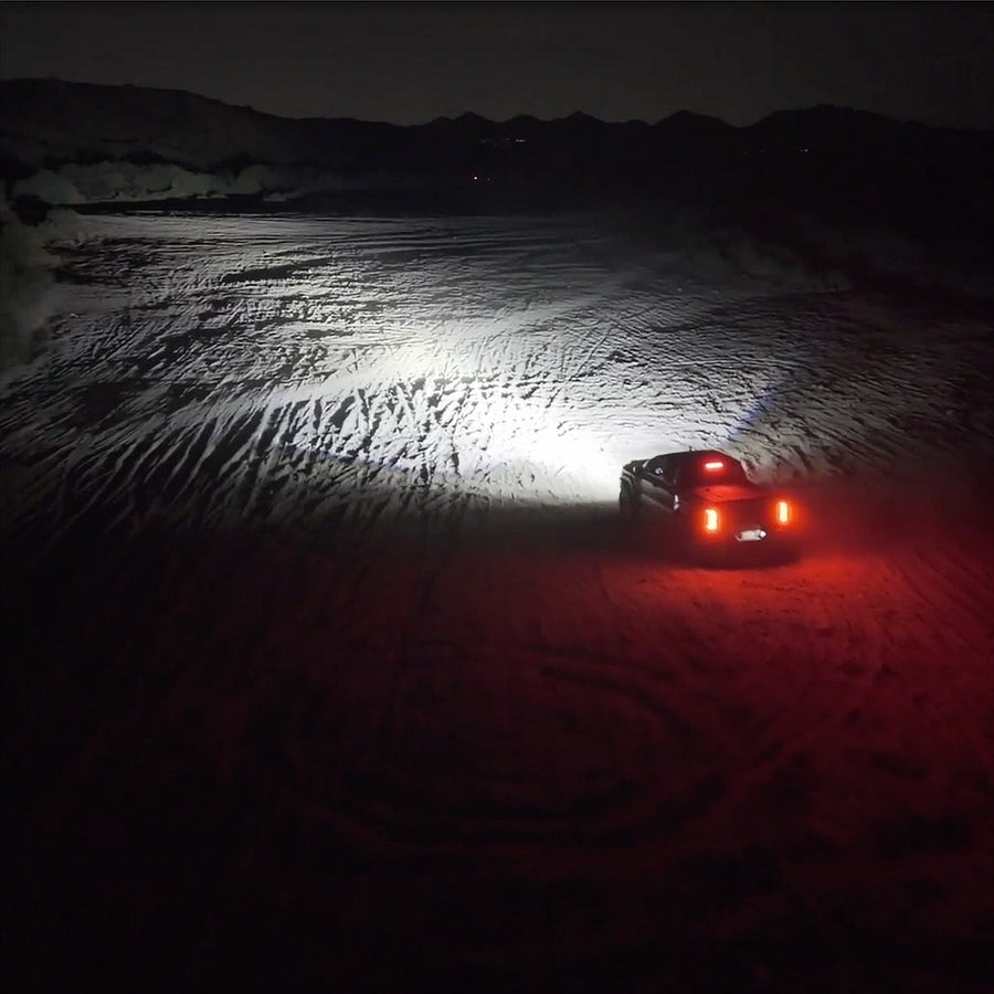 Vehicle-Specific Light Kits by Rigid: Night aerial view of a vehicle in the desert casting a wide white light beam across the sand