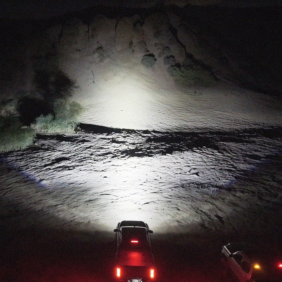 Vehicle-Specific Light Kits by Rigid: Night shot from behind a vehicle whose light bar throws a bright white beam onto a sandy desert hillside