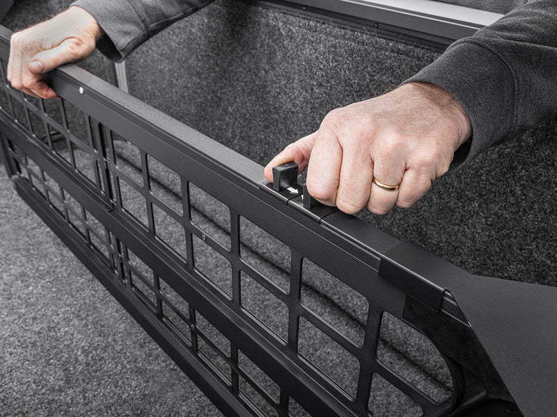 Hands gripping the Roll-N-Lock Cargo Manager grab handle to reposition it inside a carpeted bed