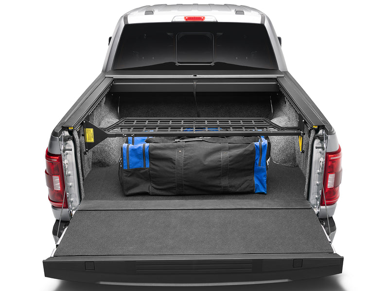 Roll-N-Lock Cargo Manager raised mid-bed holding a duffel forward, yellow operating labels on both arms