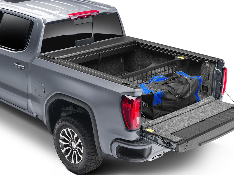 Roll-N-Lock Cargo Manager raised across an open pickup bed holding a duffel against the bulkhead, tailgate down