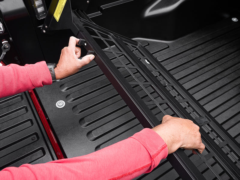 Two gloved hands seating the Roll-N-Lock Cargo Manager foot into the bed rail channel